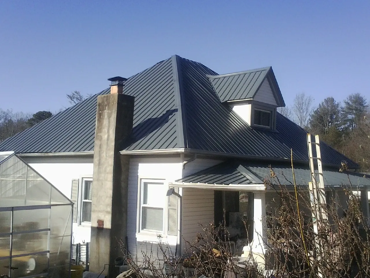 Dark blue standing seam metal roof on a white farmhouse with dormer — Slate & Tile Roof Repair by Roofing Brothers in Alpena