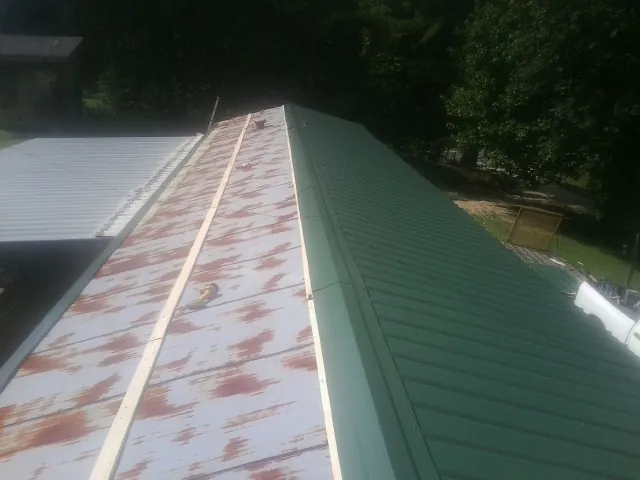 Old rusted panels beside newly installed green metal roofing — Wind Damage Roof Repair by Roofing Brothers in Alpena