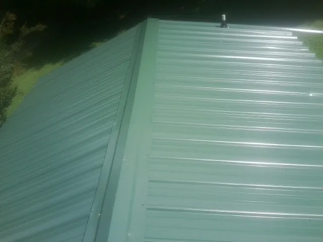 New green metal panels meeting at the ridge of a roof — Flat Roof Repair work by our crew in Alpena