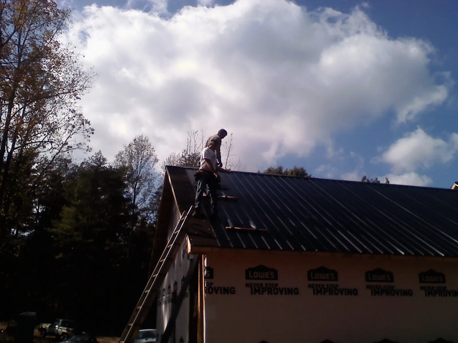 Roofer fastening dark metal panels high against a cloudy sky, from a Roof Inspection job in Alpena