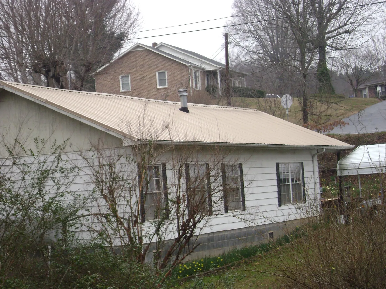 Tan metal roof on a white sided house set into a hillside — Commercial Roofing by Roofing Brothers in Alpena