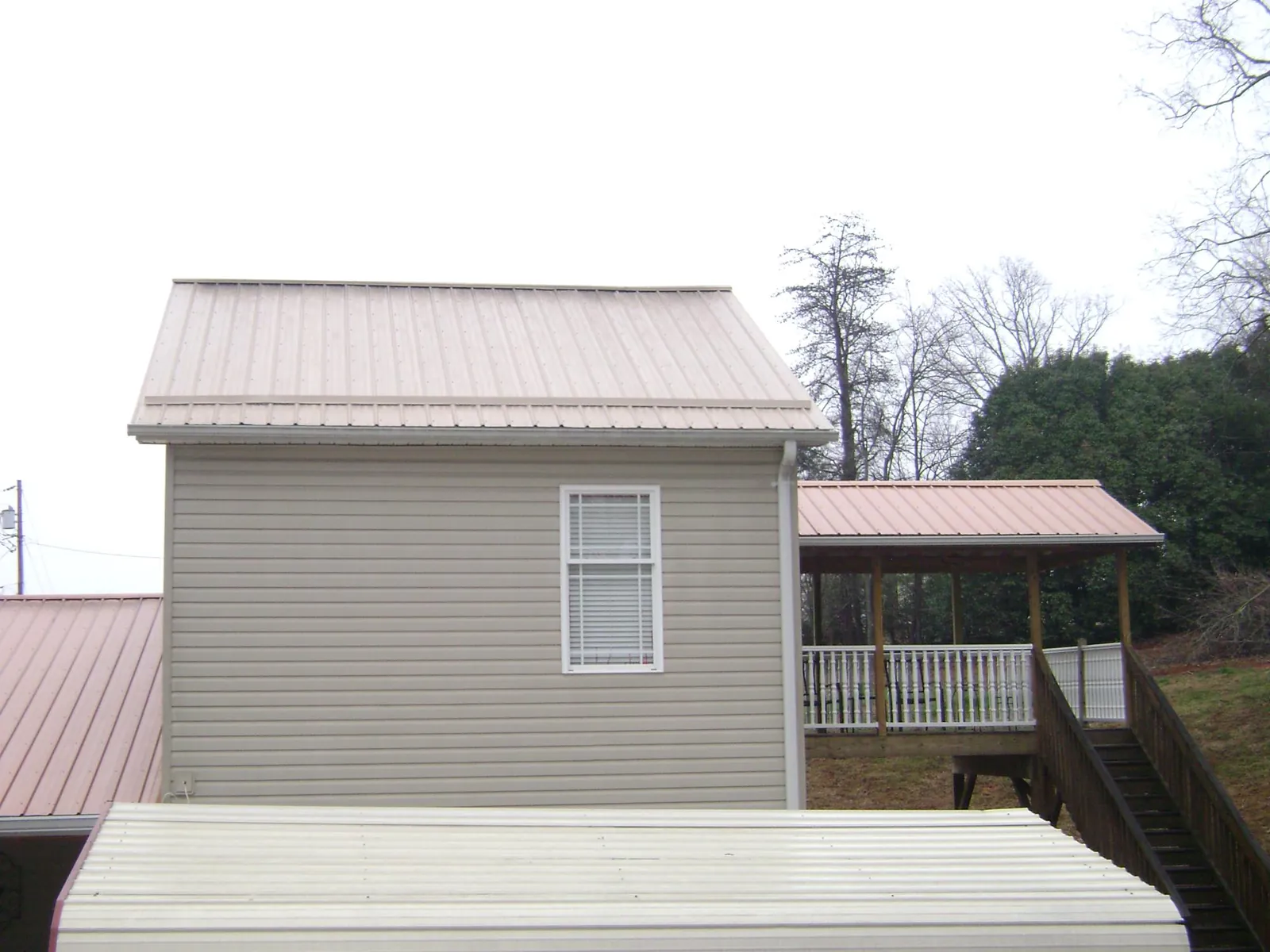 Tan metal roofs on a two story addition and attached porch, from a Roof Replacement job in Alpena